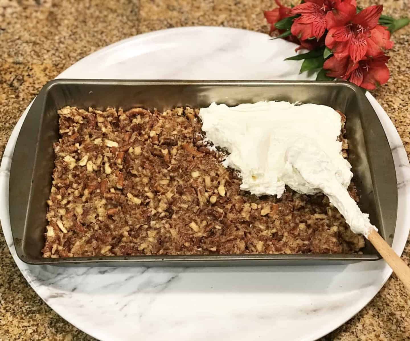 Whipped cream cheese filling being spread over the cooled pretzel crust to create the creamy middle layer of strawberry pretzel salad.
