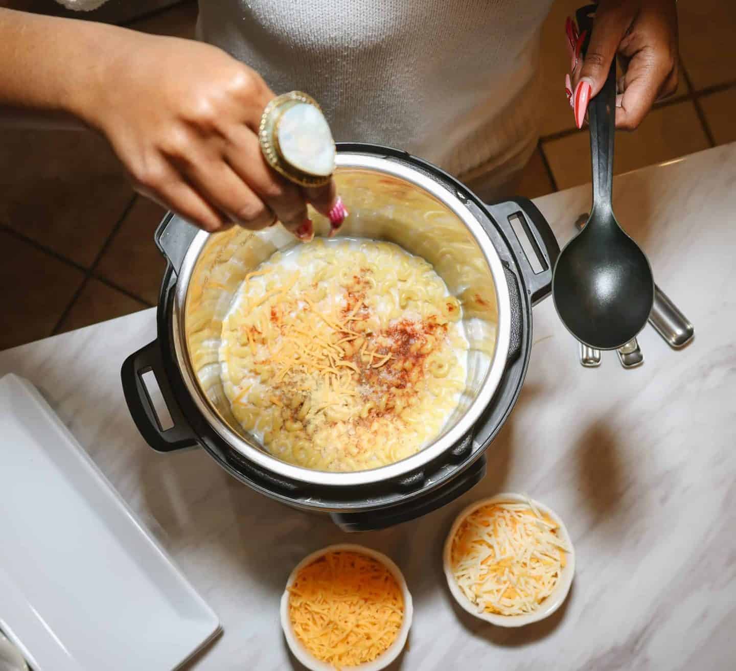 Seasoning creamy soul food macaroni and cheese in an Instant Pot, showcasing modern soul food cooking techniques rooted in Black food culture and perfectly balanced flavor &mdash; The Soul Food Pot&reg; Ultimate Soul Food Recipes Guide.