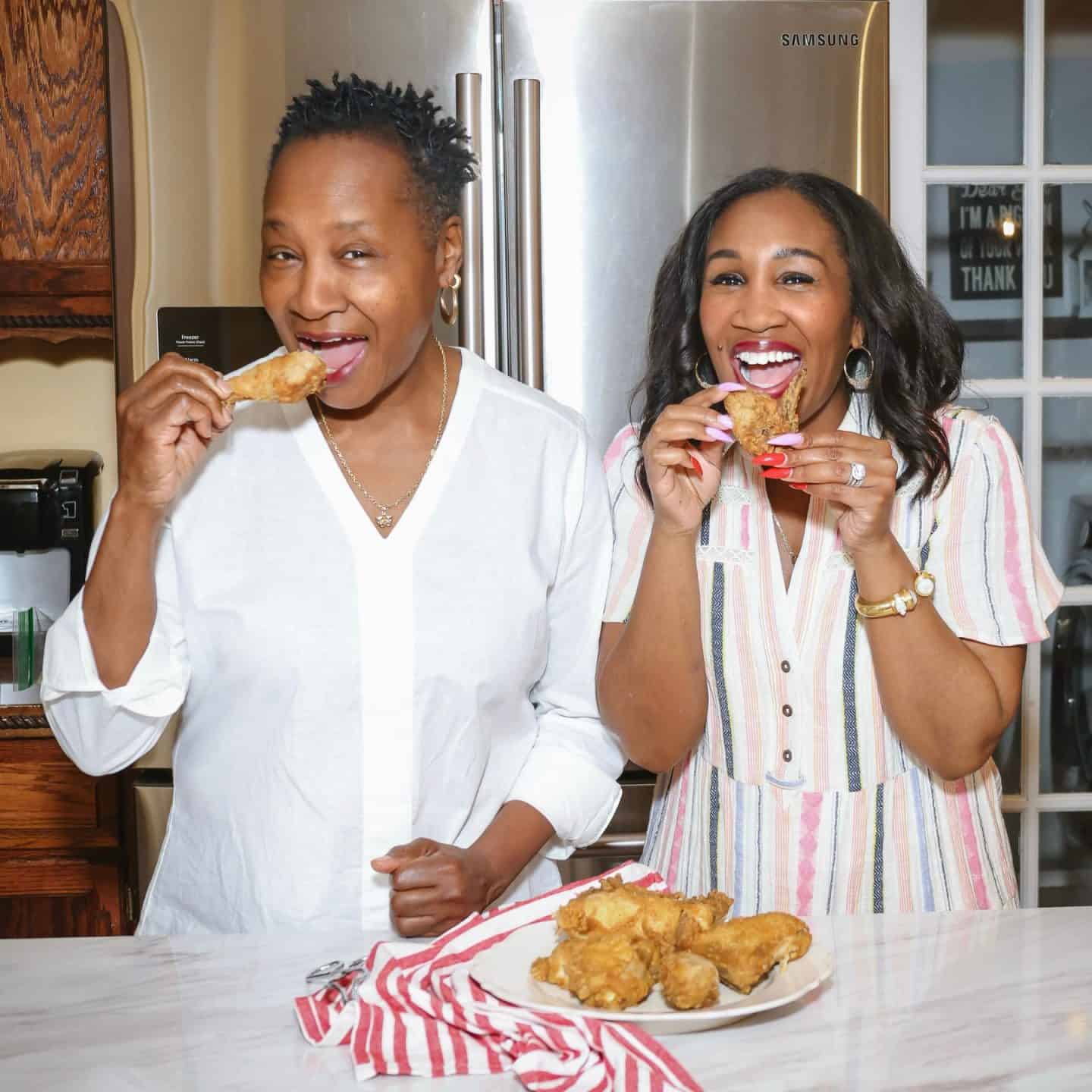 Soul food vs Southern food - history, identity, and the difference: Two Black women, Shaunda Necole of The Soul Food Pot&reg;, and her mom are joyfully eating fried chicken together in her kitchen, highlighting African American soul food traditions and the cultural distinction between soul food and Southern cuisine.