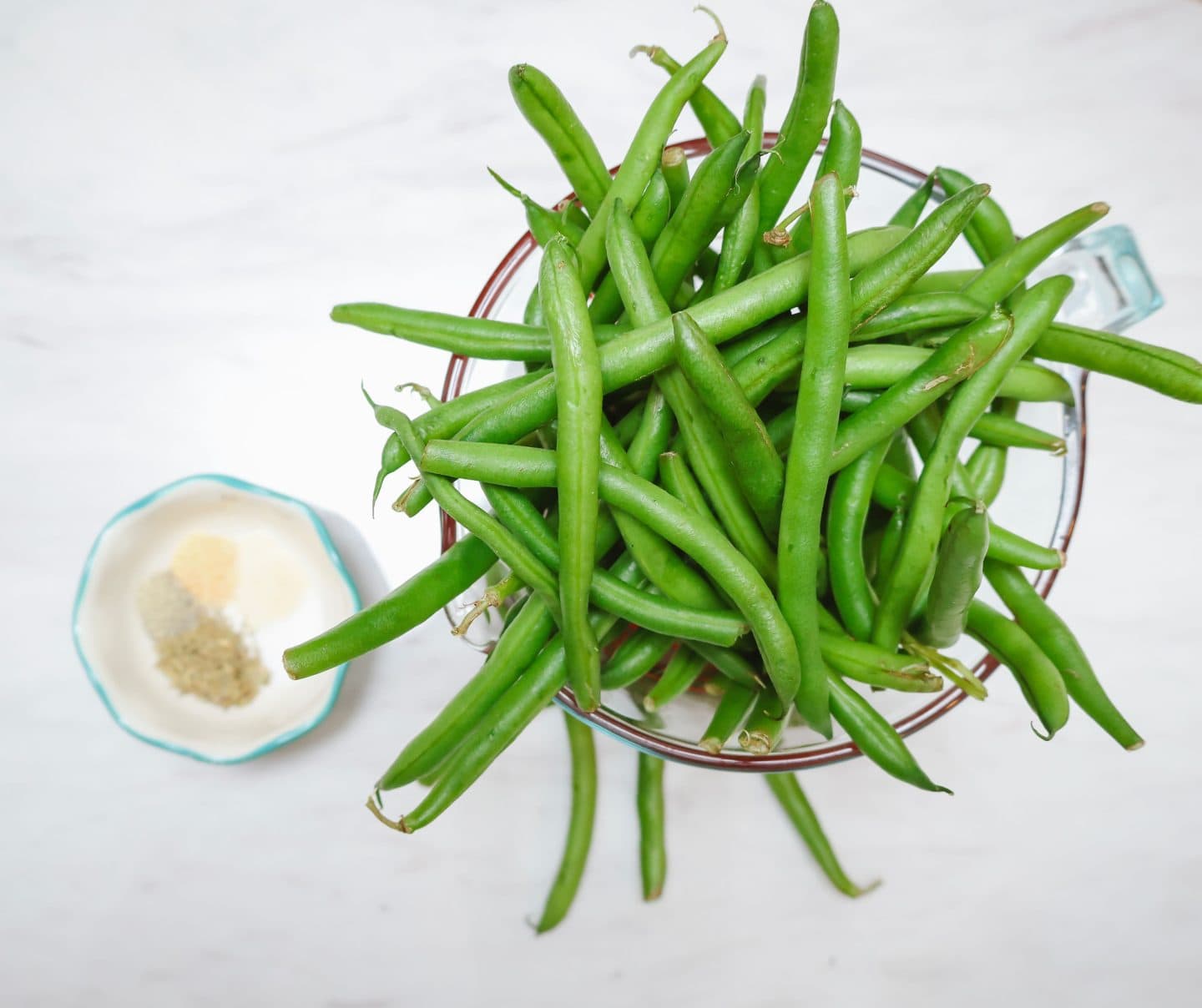 Fresh whole green beans in a bowl with garlic powder, thyme, salt, and black pepper — the classic flavor foundation for Southern soul food green beans by The Soul Food Pot®.