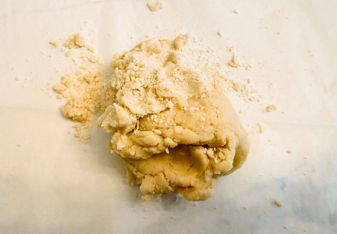 Sweet potato pie crust dough at the crumbly stage before forming into a disc — illustrating proper hydration and mixing to avoid tough or overworked pastry.