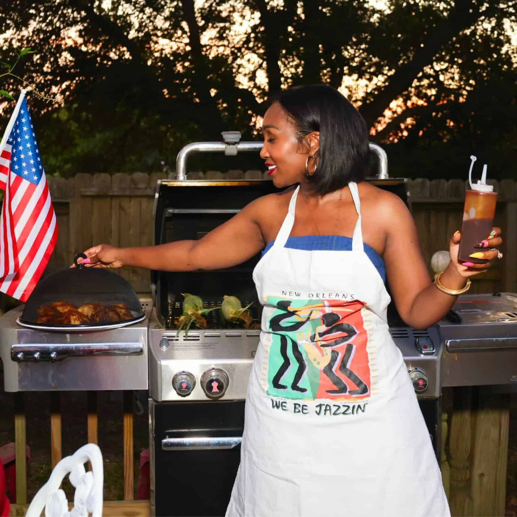 Shaunda Necole grilling soul food barbecue in her backyard while hosting a Southern cookout, wearing a Juneteenth apron beside a backyard grill with BBQ chicken, an American flag, and classic Black cookout favorites.