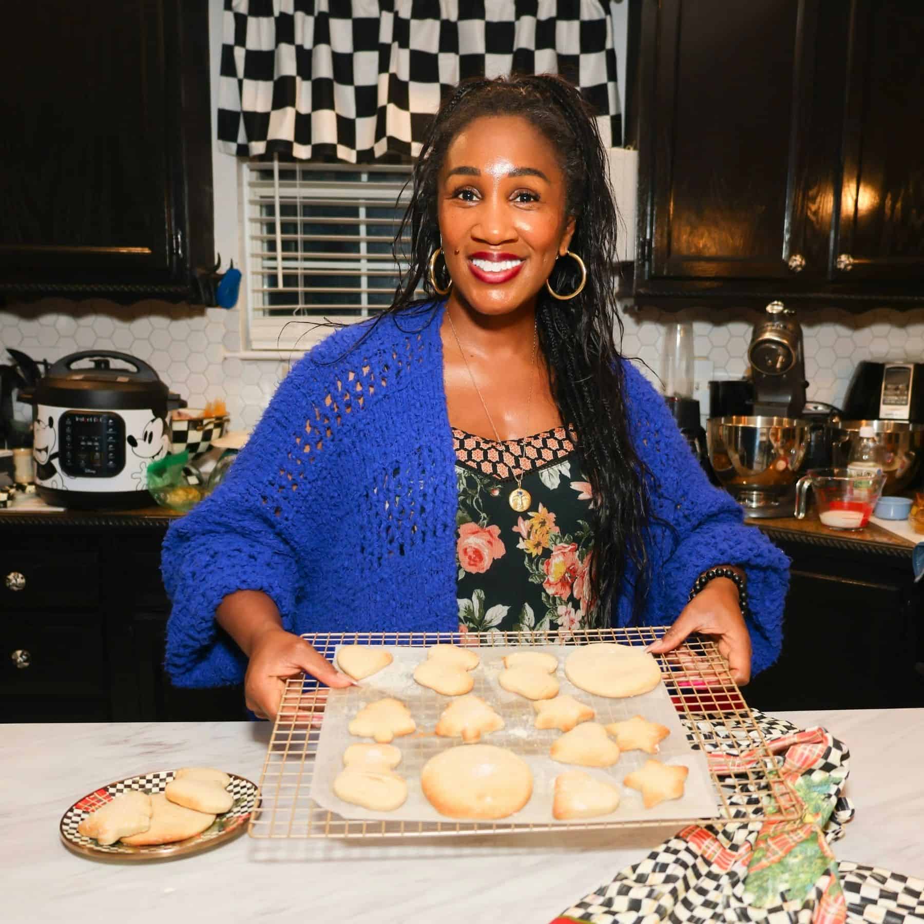Shaunda Necole, founder of The Soul Food Potยฎ, smiling in her kitchen while holding a cooling rack of freshly baked Christmas cookies, including tree, star, heart, and round sugar cookies. The image celebrates Southern holiday baking traditions and soul food Christmas recipes, helping families preserve Black culinary heritage through festive homemade treats.