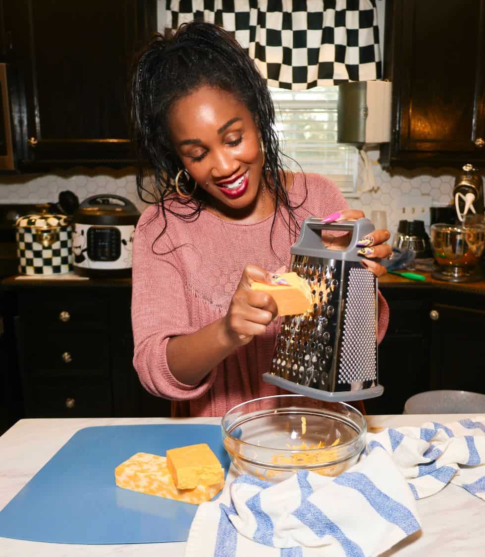 Shaunda Necole grating cheddar cheese by hand while preparing Black Folks baked mac and cheese in her kitchen for The Soul Food Pot®.
