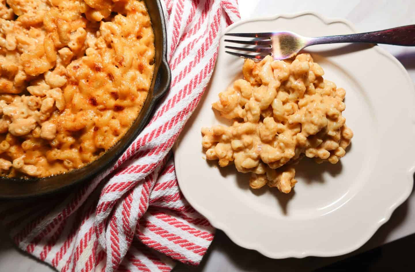 Creamy Black Folks baked mac and cheese served on a white plate beside the cast-iron skillet, a Southern soul food recipe from The Soul Food Pot®.