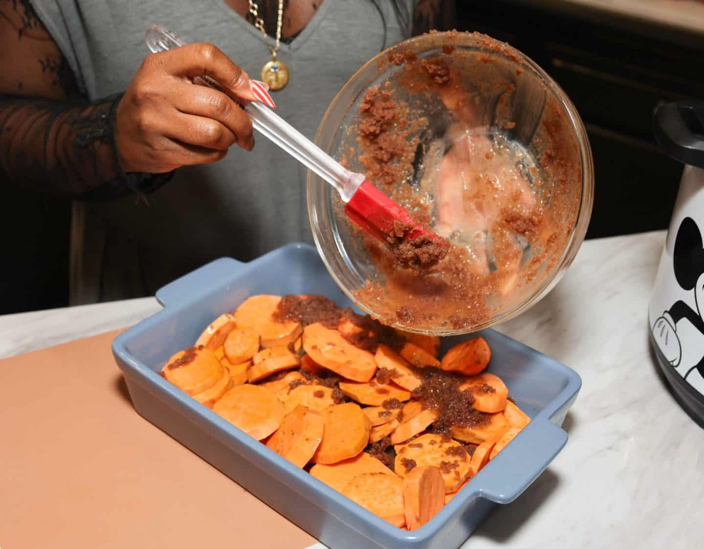 Shaunda Necole pours a buttery brown sugar spice glaze over sliced sweet potatoes in a baking dish for The Soul Food Pot® Southern candied yams recipe.