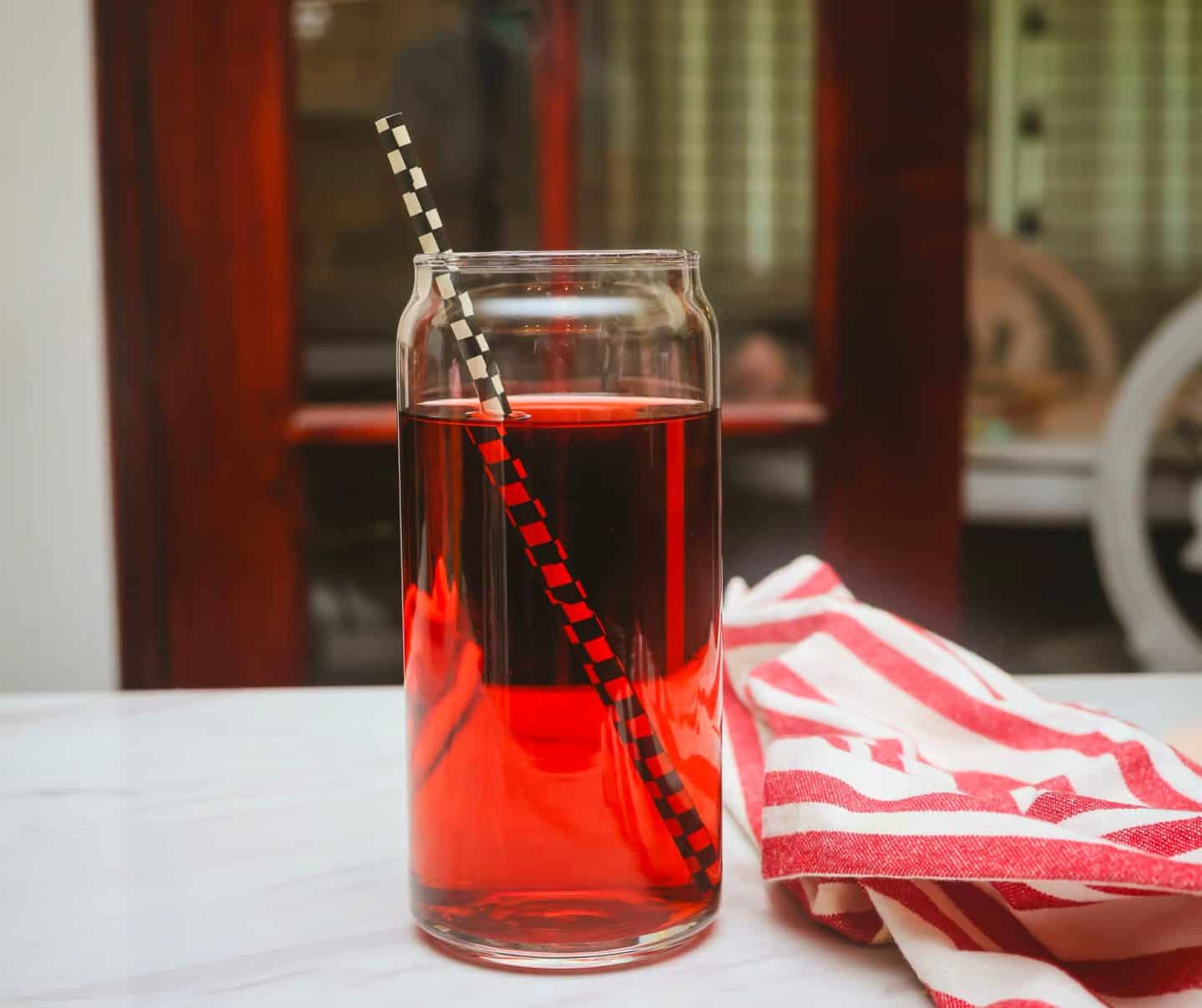 Close-up of The Soul Food Pot® Grown Folks Red Kool-Aid, a less-sweet nonalcoholic Black Cherry Kool-Aid drink served cold with a black-and-white checkered straw.
