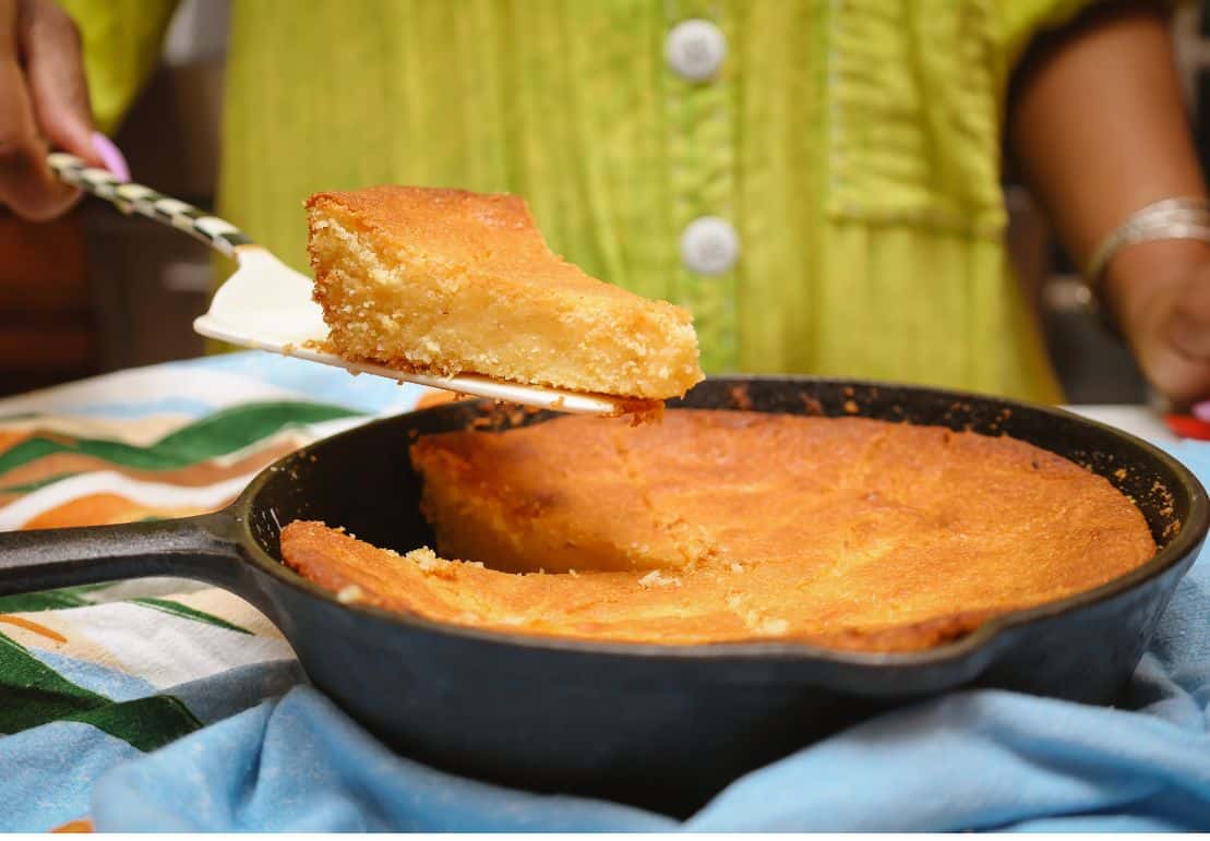 Slice of golden Southern cornbread lifted from a cast-iron skillet, showing its tender, moist crumb and crisp browned edges.