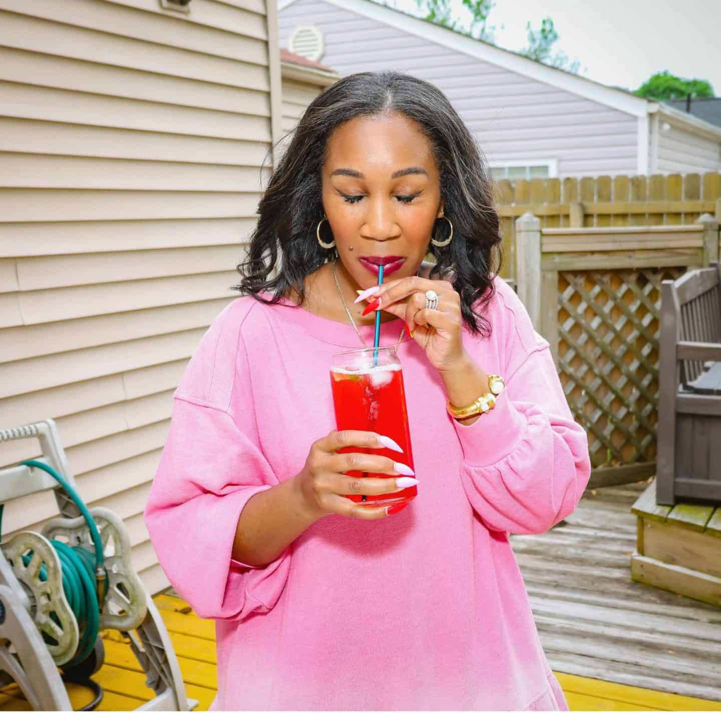Shaunda Necole sipping an iced glass of bright red Grown Folks Red Kool-Aid outdoors, an alcohol-free grown-up red drink recipe from The Soul Food Pot®.