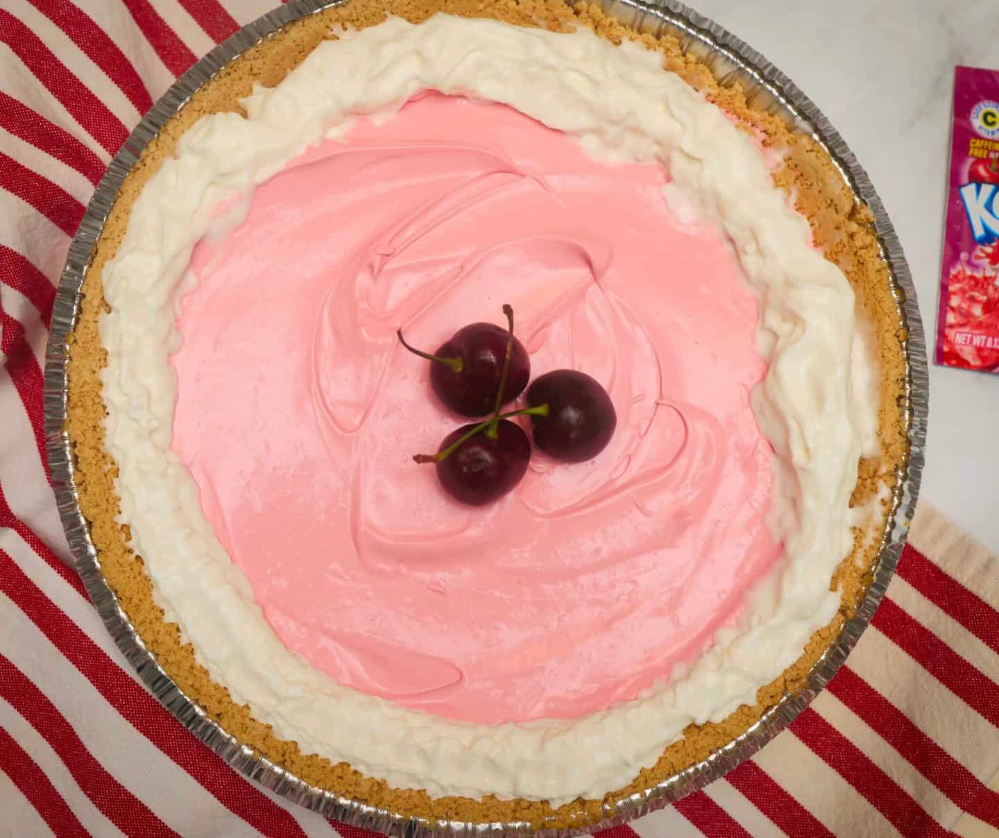 The Soul Food Pot® Red Kool-Aid Pie made with Black Cherry Kool-Aid, featuring a creamy pink no-bake filling in a graham cracker crust, topped with whipped cream and fresh cherries.