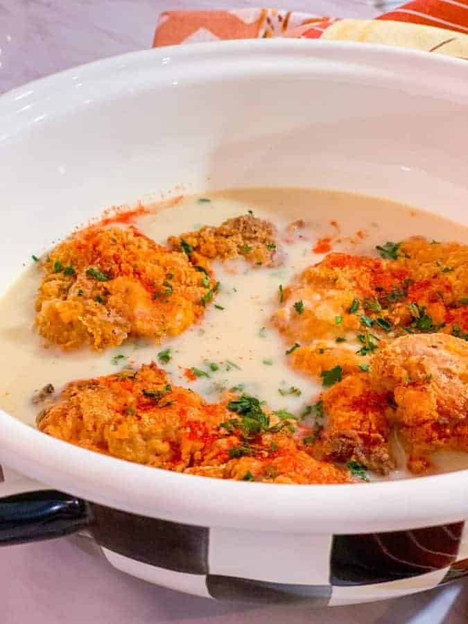 Golden battered chicken thighs sitting mostly covered in creamy gravy for Shaunda Necole’s Southern smothered chicken from The Soul Food Pot®.