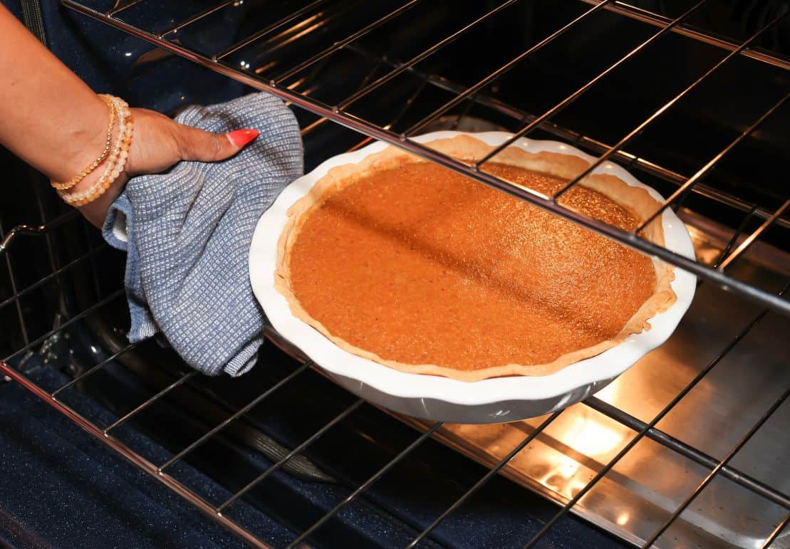 Freshly baked sweet potato pie being removed from the oven with a smooth, set custard filling and golden crust for The Soul Food Pot®.