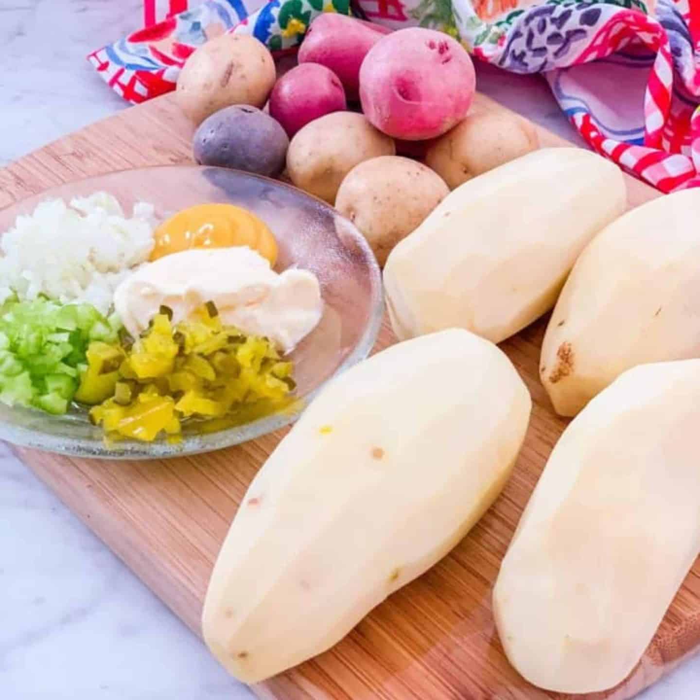 Ingredients for The Soul Food Pot's Black folks Southern potato salad, including peeled russet potatoes, small red and purple potatoes, diced vegetables, pickles, mustard, and mayonnaise.