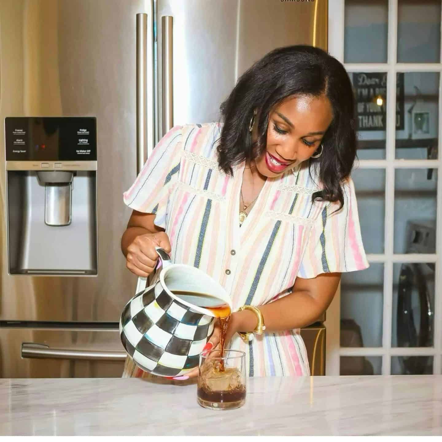Shaunda Necole pouring Southern sweet tea from a black-and-white Courtly Check pitcher into a glass of ice, a classic cookout drink from The Soul Food Pot®.