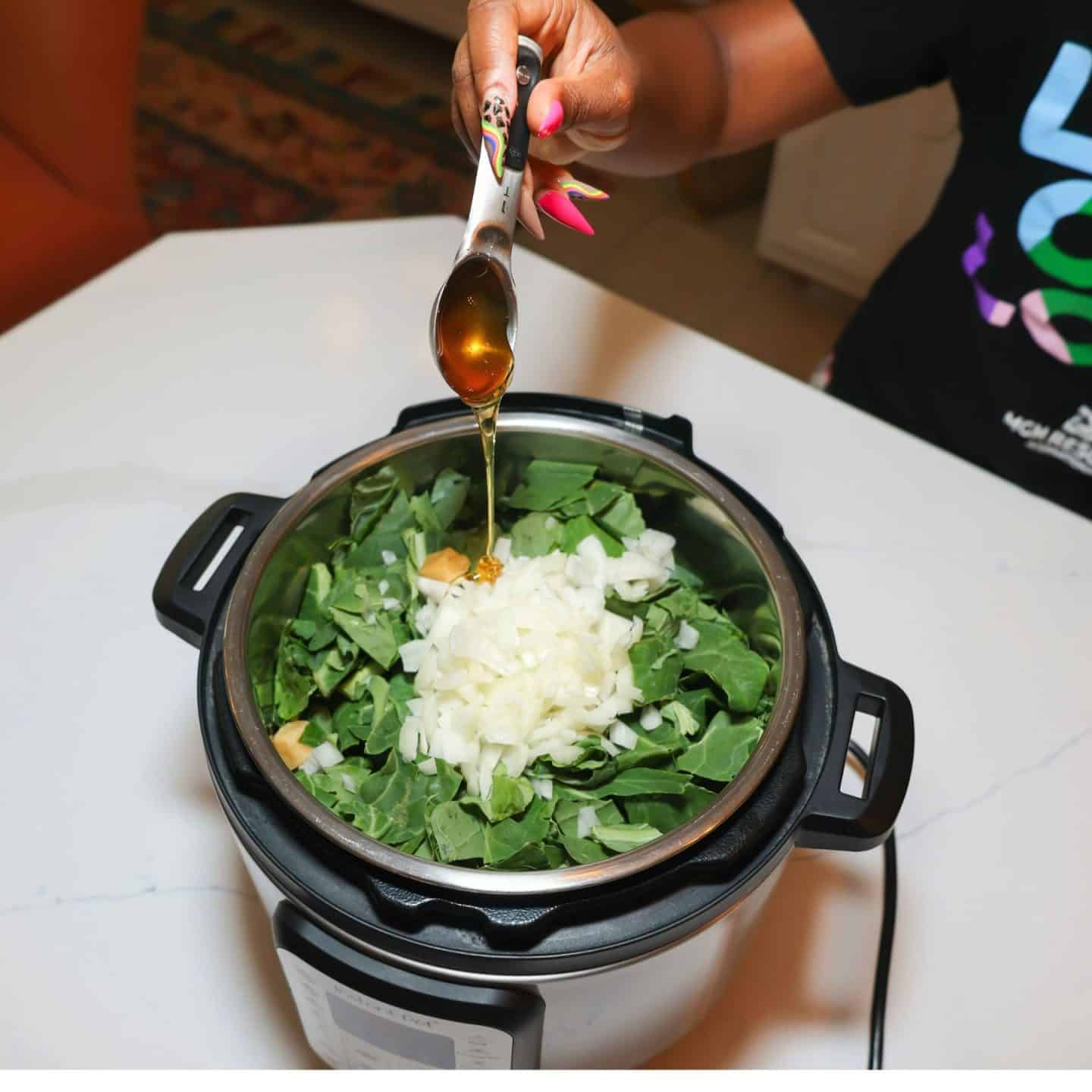 Seasoning being poured from a measuring spoon over chopped collard greens and onions in an Instant Pot for The Soul Food Pot® collard greens recipe.