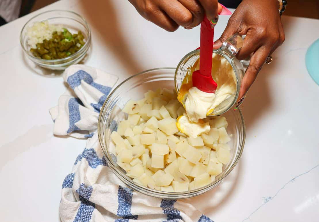 Shaunda Necole adding mayonnaise and mustard to chopped potatoes for Southern potato salad.