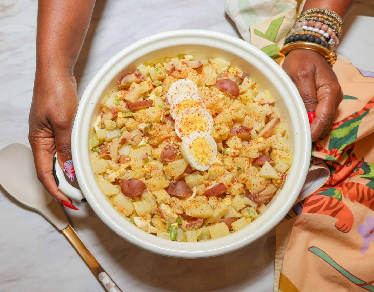 Shaunda Necole holding a white bowl of Black folks Southern potato salad with red-skinned potatoes, sliced hard-boiled eggs, celery, and paprika.