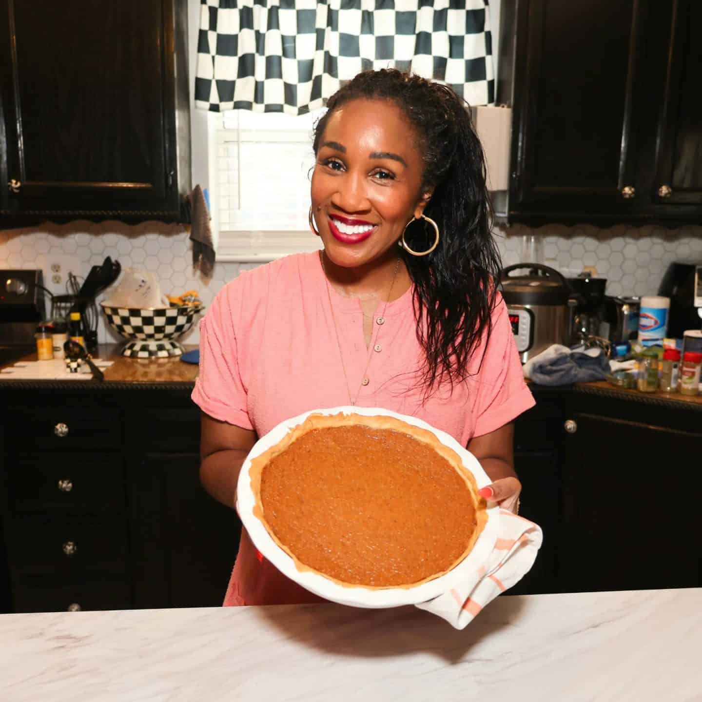 Shaunda Necole smiling in her home kitchen while holding her freshly baked Black Folks Sweet Potato Pie™ in a ruffled pie dish, featuring a golden crust and smooth, spiced custard filling.