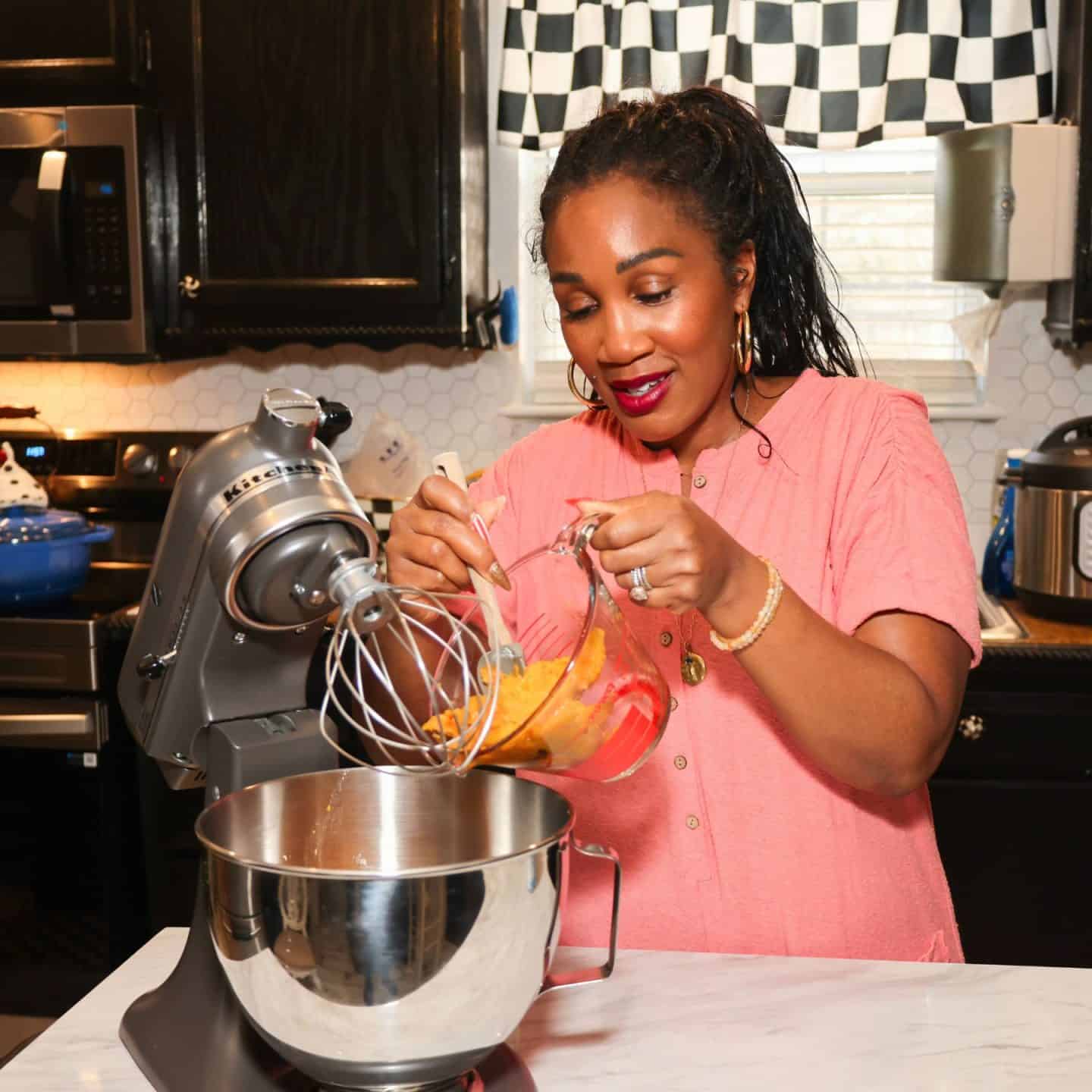 Shaunda Necole transferring cooked sweet potato flesh from a glass measuring cup into a KitchenAid stand mixer bowl to prepare her Black Folks Sweet Potato Pie™ filling.