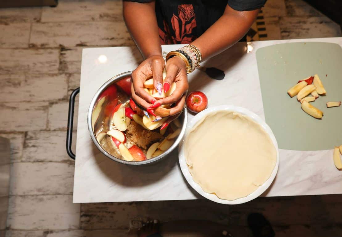 Shaunda Necole prepares sliced red apples beside a double pie crust for her soulful apple pie recipe from The Soul Food Pot®.