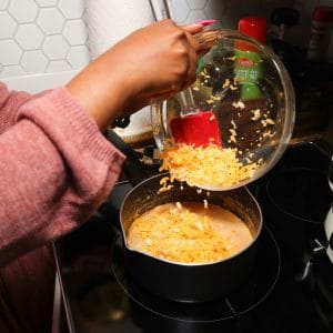 Shredded cheese being added to a seasoned sauce