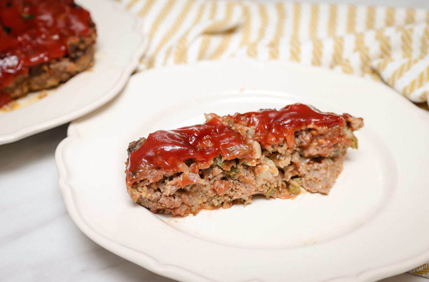 Slice of tender Southern meatloaf with vegetables and tomato glaze served on a white plate from The Soul Food Pot®