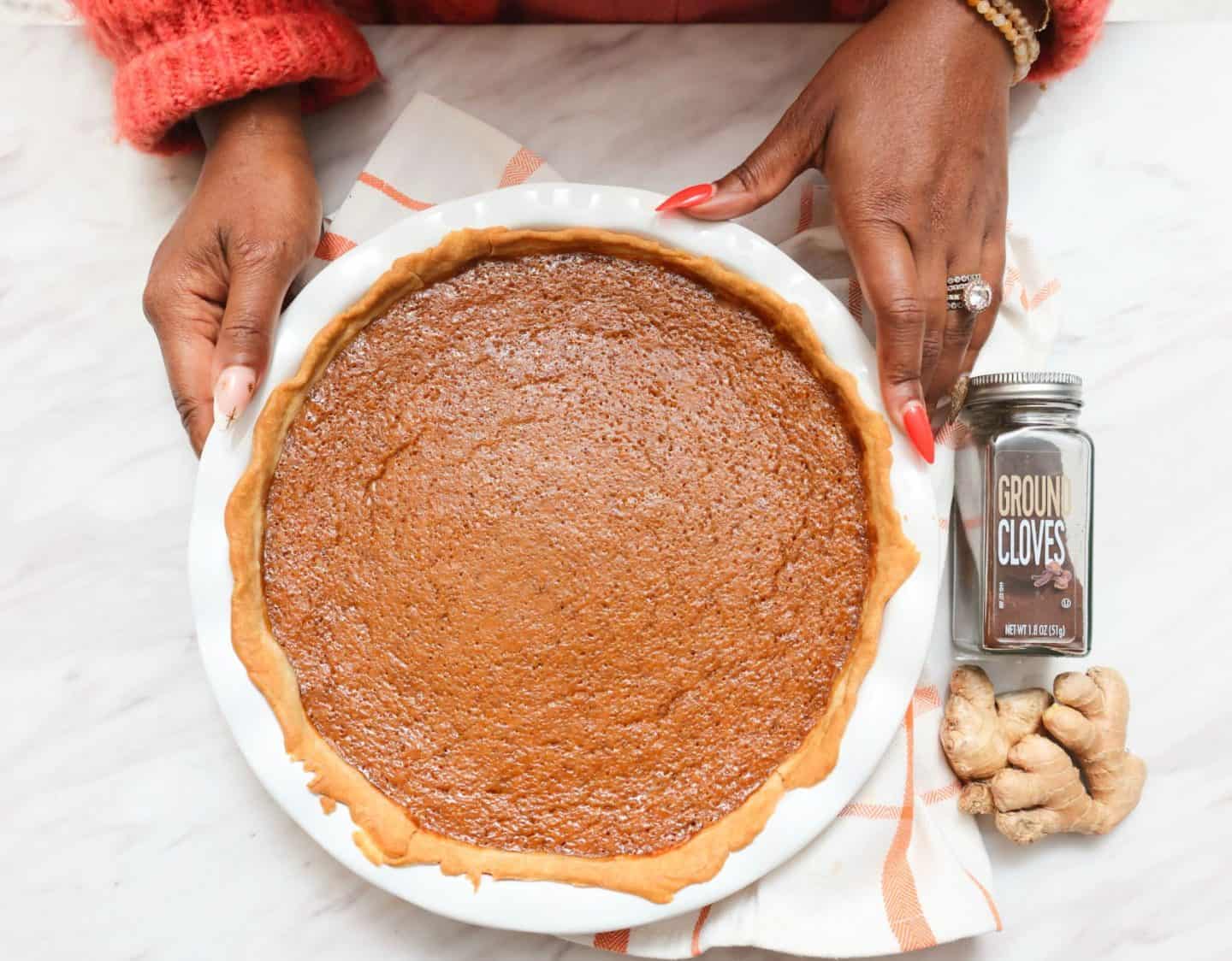 Black folks’ sweet potato pie beside ground cloves and fresh ginger, two of Shaunda Necole’s signature spices for The Soul Food Pot® recipe.
