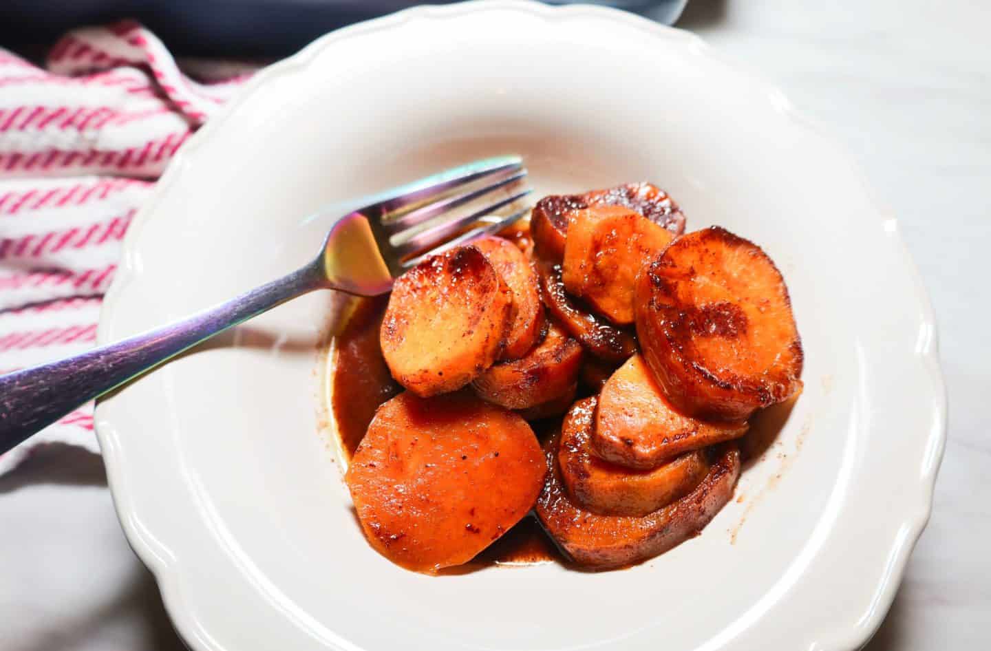 Tender stovetop candied yams coated in thick, glossy brown sugar and spice syrup after cooking.