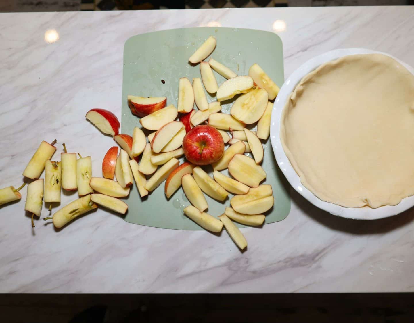 Thick red apple slices with the peels left on beside a prepared bottom pie crust for Shaunda’s rustic Southern apple pie.