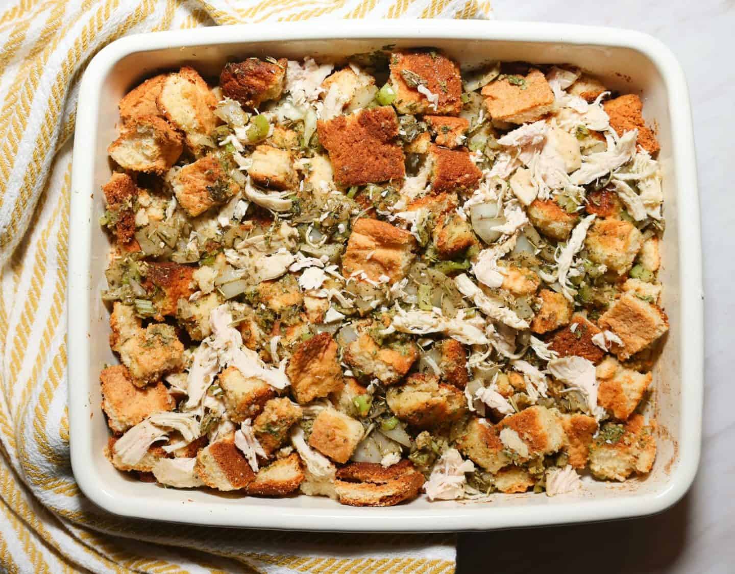 Unbaked Black folks chicken and dressing with visible cornbread cubes, shredded chicken, onion, celery, and herbs before baking, from The Soul Food Pot®.