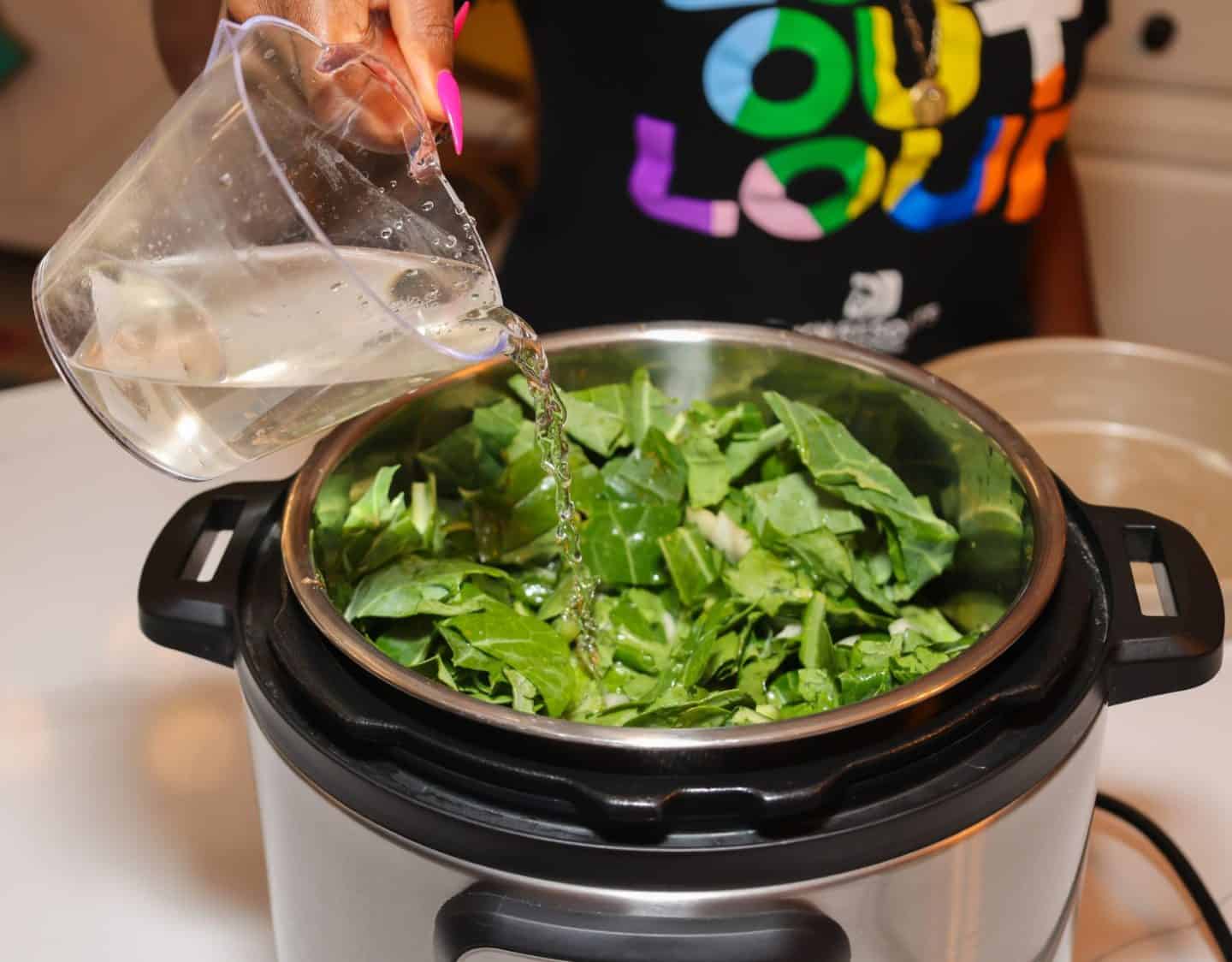 Water being poured over chopped fresh collard greens in an Instant Pot while preparing The Soul Food Pot® Southern collard greens recipe.