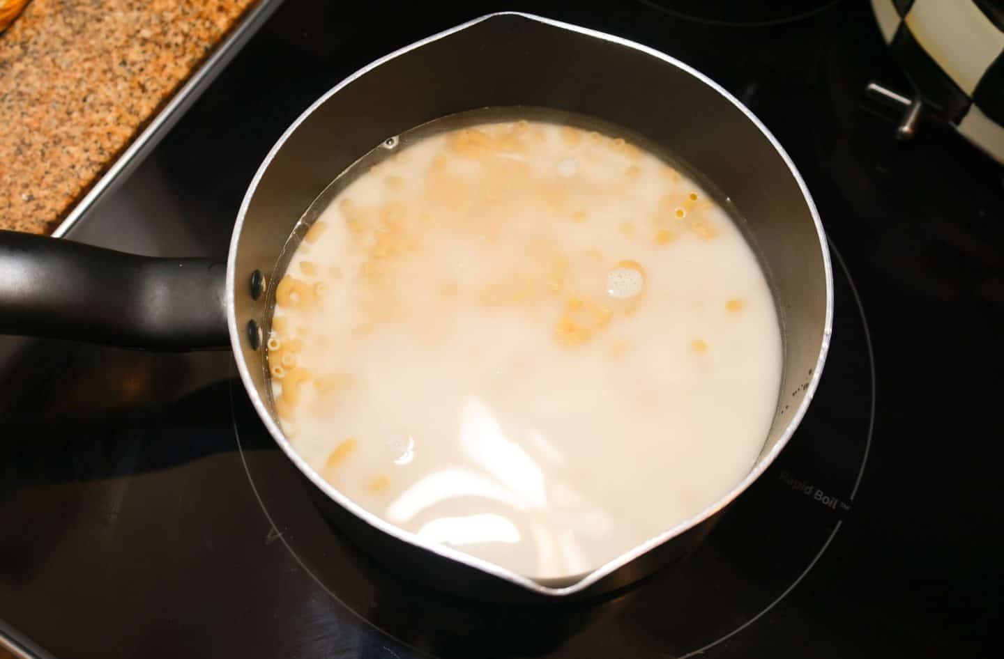 Elbow macaroni cooking in a mixture of milk and water in a saucepan, the first step in The Soul Food Pot® baked mac and cheese recipe.