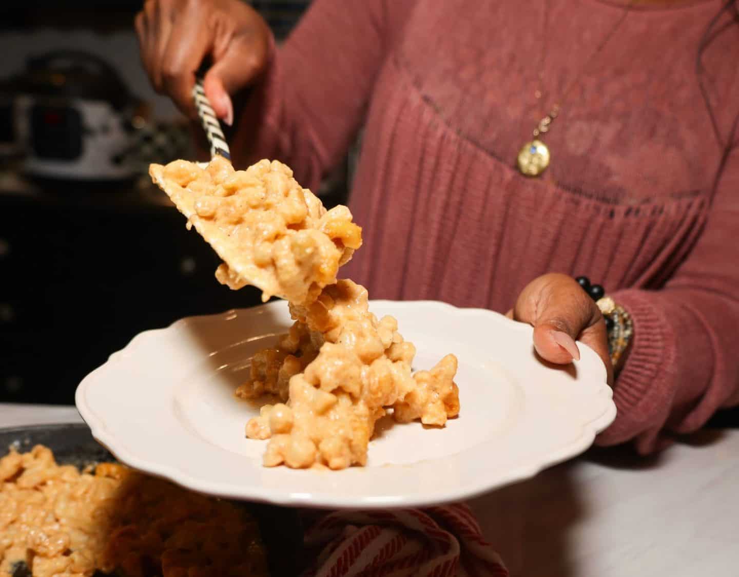 Shaunda Necole serving creamy Southern mac and cheese onto a dinner plate, a cookout side that can be reheated and enjoyed again as a Labor Day leftover from The Soul Food Pot®.
