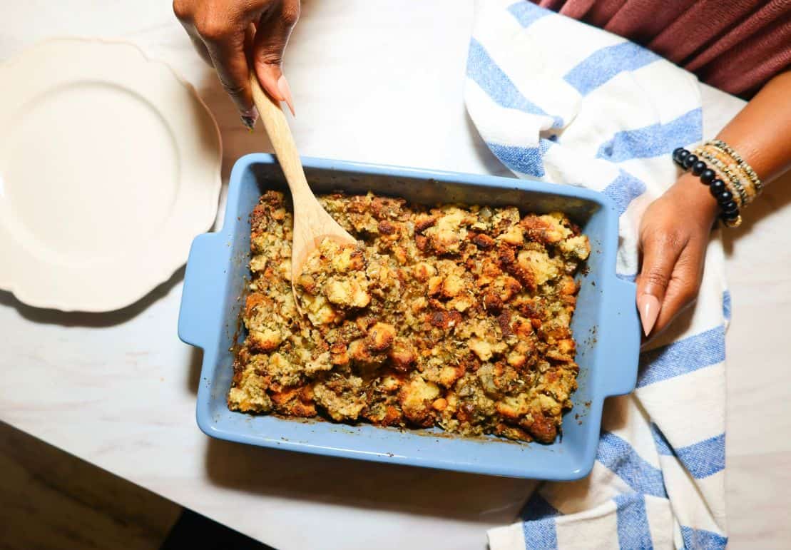 Serving homemade Black folks’ cornbread dressing from a blue baking dish, showing the golden herb-seasoned cornbread texture of The Soul Food Pot® recipe.