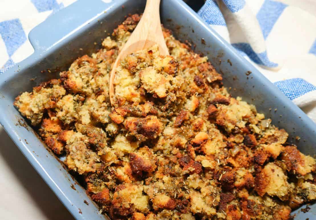 Black folks’ cornbread dressing by The Soul Food Pot®, baked golden with visible seasoned cornbread pieces and served with a wooden spoon.