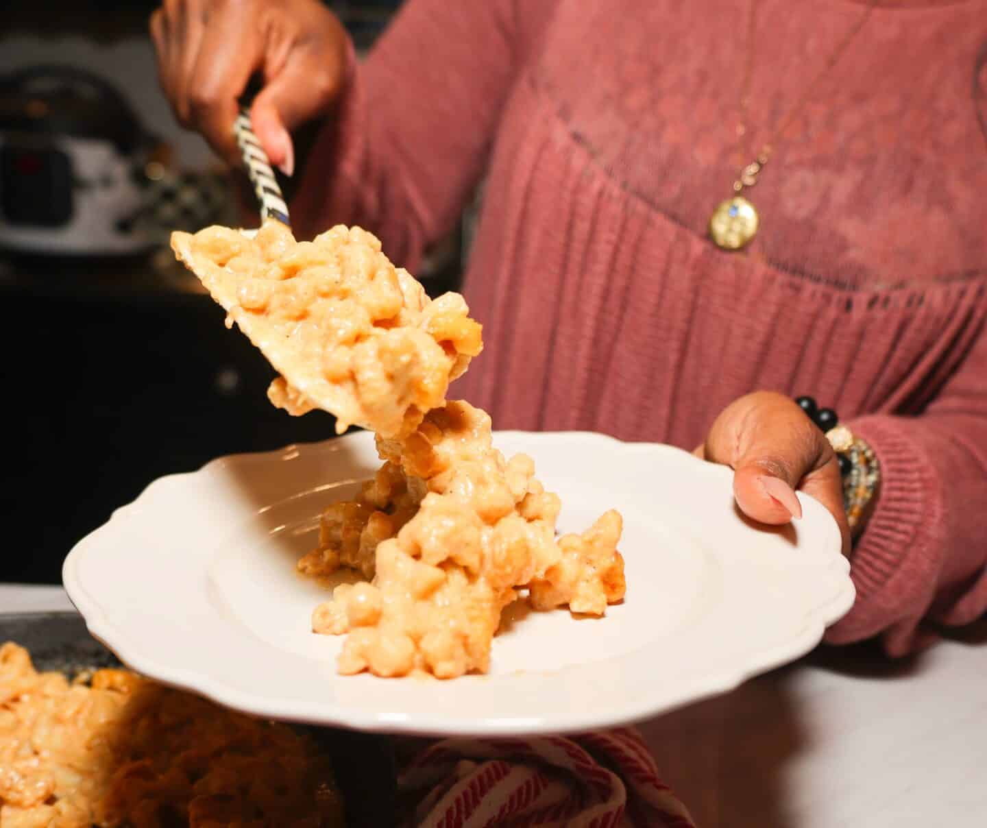 Shaunda Necole serving creamy baked macaroni and cheese onto a plate, a seasoned classic on her soul food Thanksgiving table for The Soul Food Pot®.